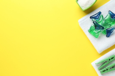 Photo of Laundry capsules, washing powder, towels and clothespins on yellow background, flat lay. Space for text