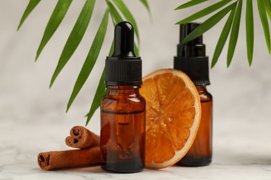 Photo of Bottles of organic cosmetic products, cinnamon sticks, dried orange slice and green leaves on light background