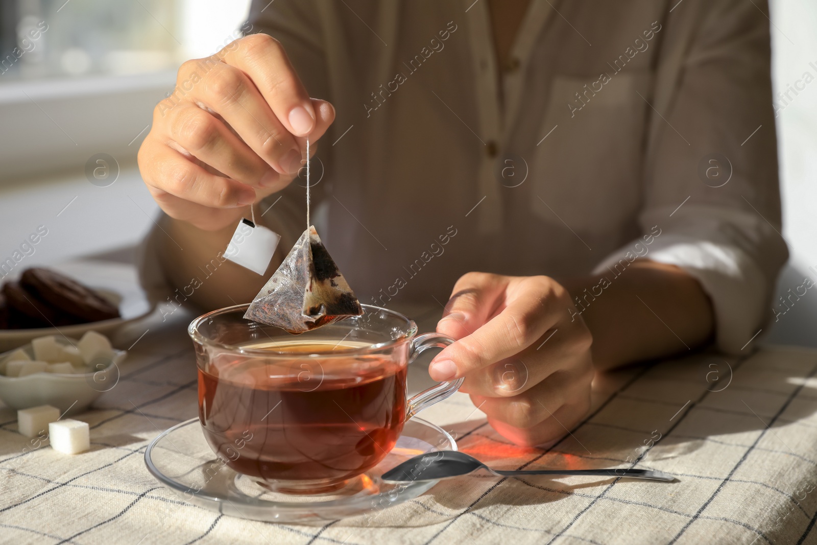 Photo of Woman taking tea bag out of cup at table indoors, closeup