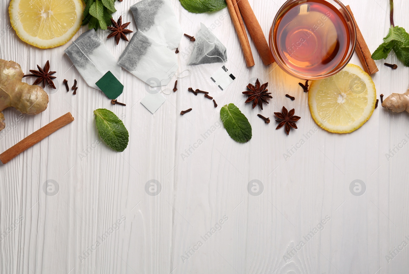 Photo of Tea bags, cup of hot drink and ingredients on white wooden table, flat lay. Space for text