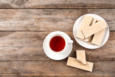 Photo of Delicious wafers with cup of tea on brown wooden background, top view. Space for text