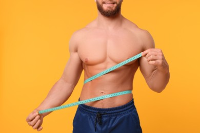 Photo of Athletic man measuring waist with tape on orange background, closeup. Weight loss concept