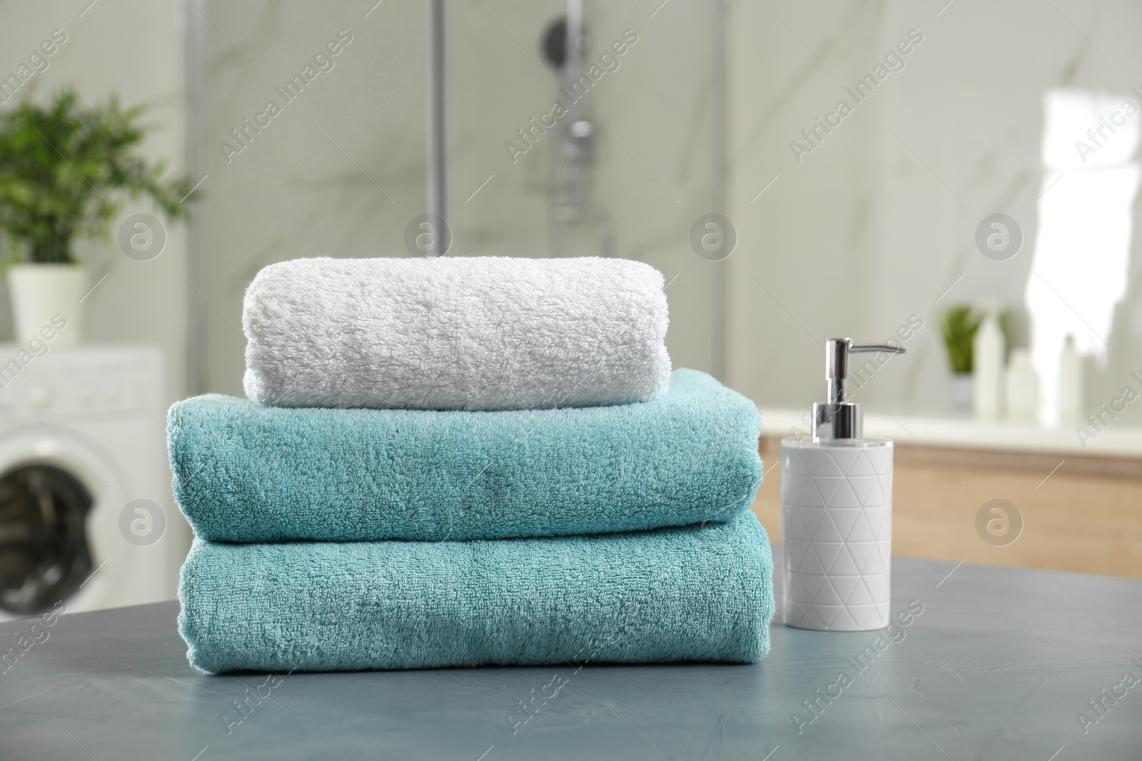 Photo of Stack of clean towels and soap dispenser on grey stone table in bathroom