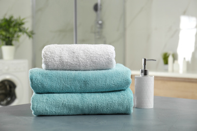 Stack of clean towels and soap dispenser on grey stone table in bathroom