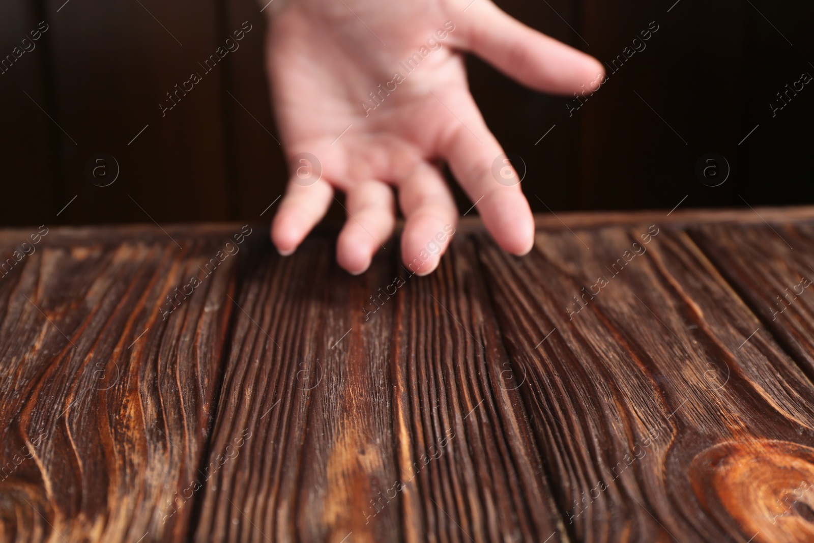 Photo of Woman holding hand above wooden table, selective focus. Space for text