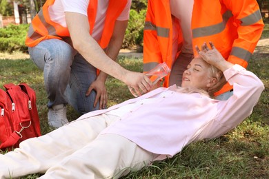Photo of Workers with bottle of water helping mature woman in park. Suffering from heat stroke