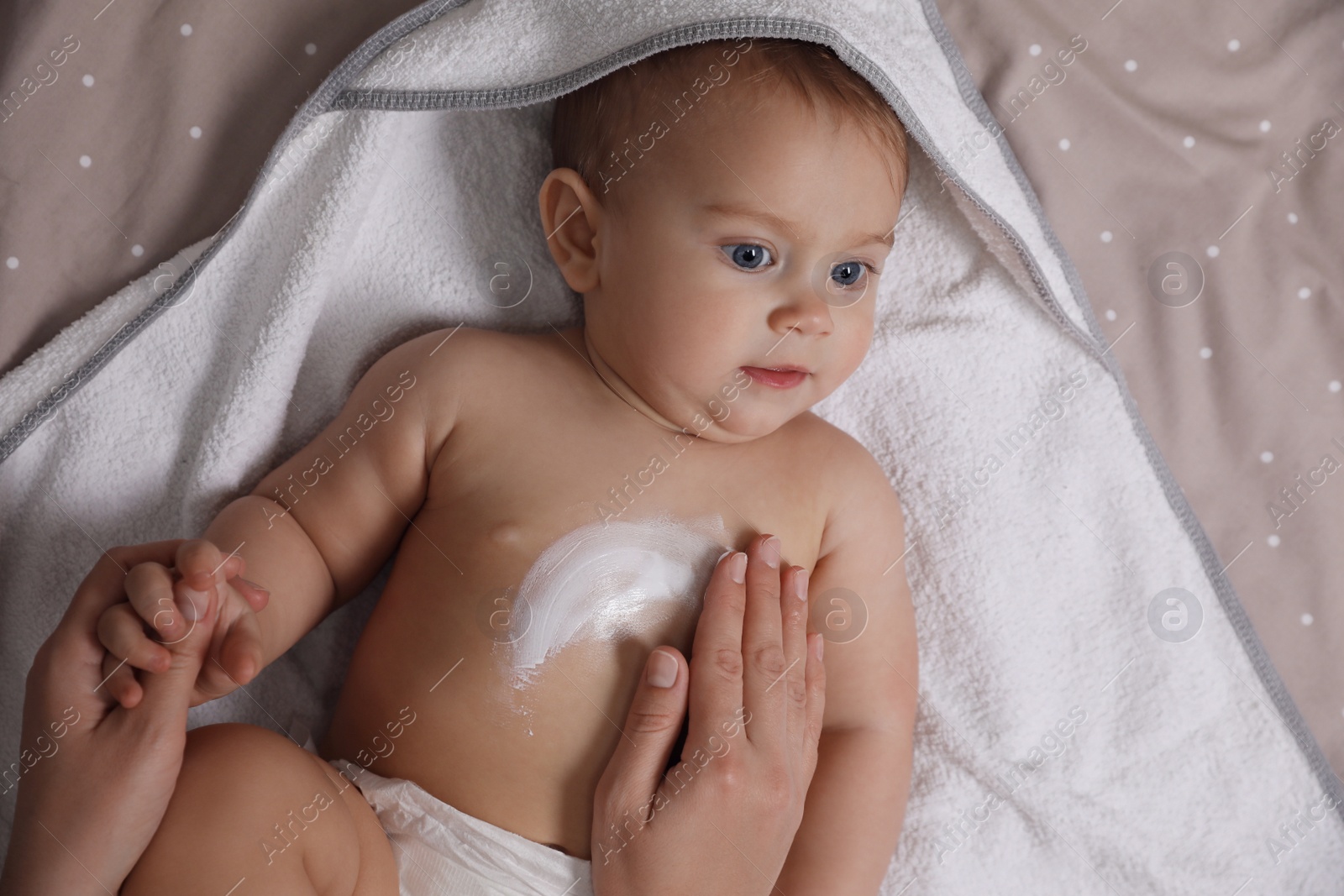 Photo of Mother applying moisturizing cream onto her little baby's skin on bed, closeup