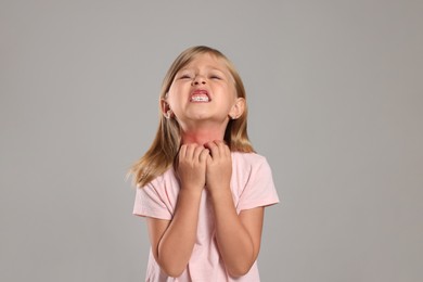 Photo of Suffering from allergy. Little girl scratching her neck on light gray background