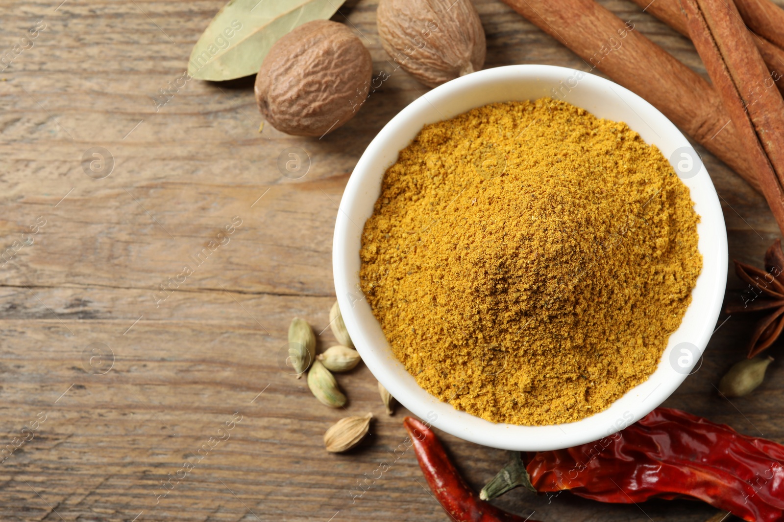 Photo of Dry curry powder in bowl and other spices on wooden table, flat lay. Space for text