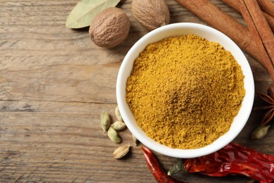 Photo of Dry curry powder in bowl and other spices on wooden table, flat lay. Space for text