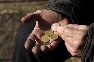 Photo of Poor homeless man holding coins outdoors, closeup