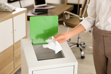 Young woman throwing paper into recycling bin at office, closeup