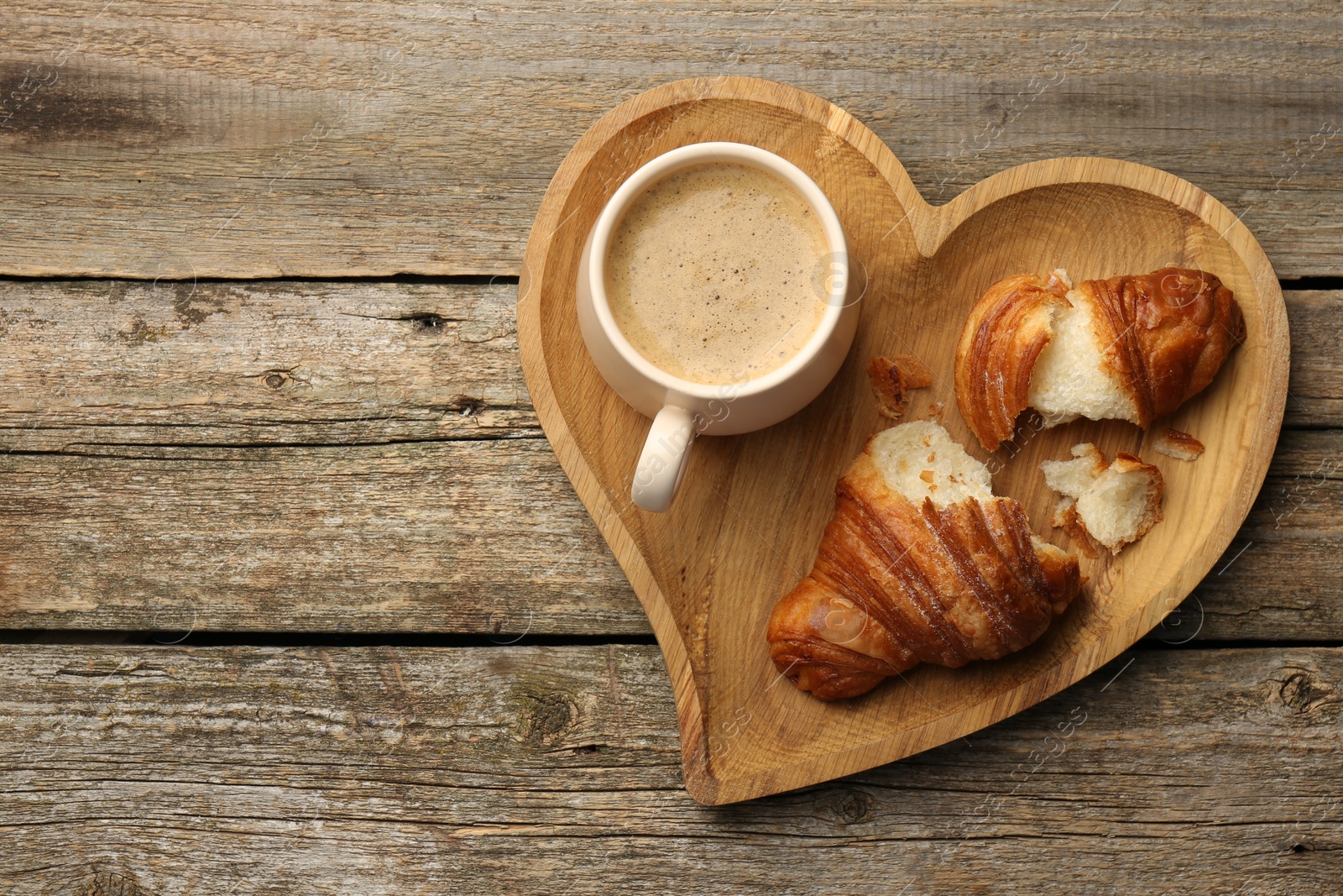 Photo of Delicious fresh croissant and cup of coffee on wooden table, top view. Space for text