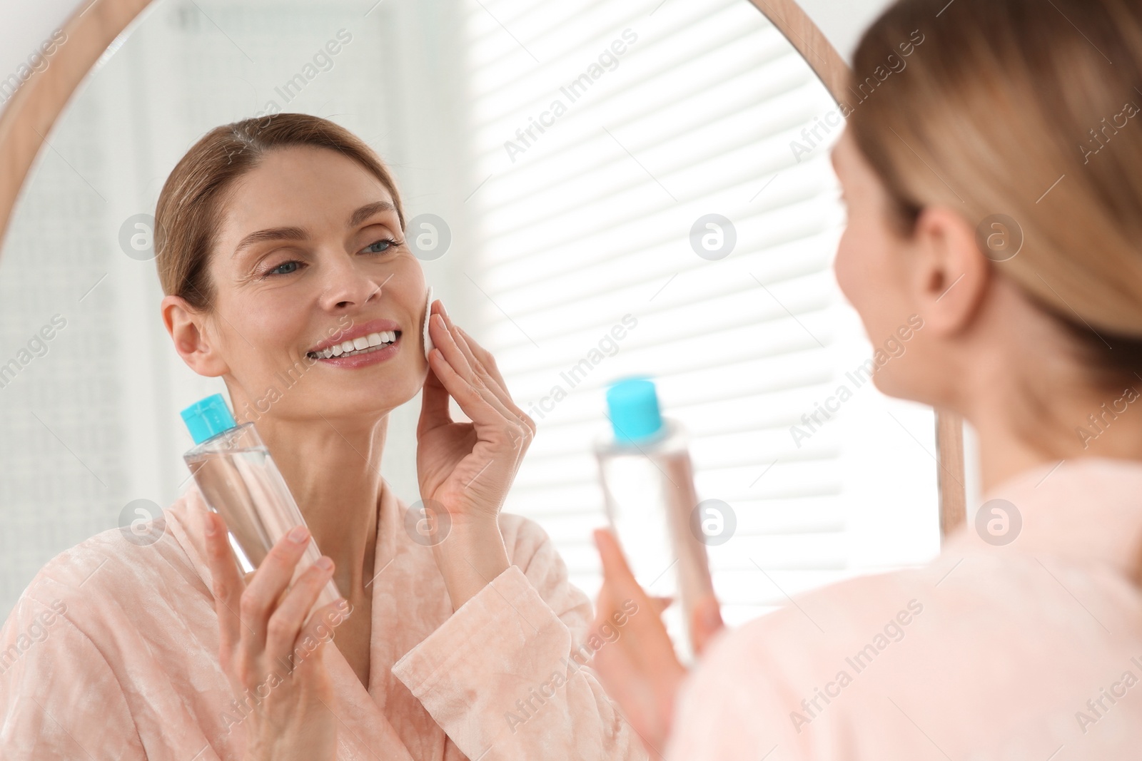 Photo of Beautiful woman removing makeup with cotton pad near mirror indoors