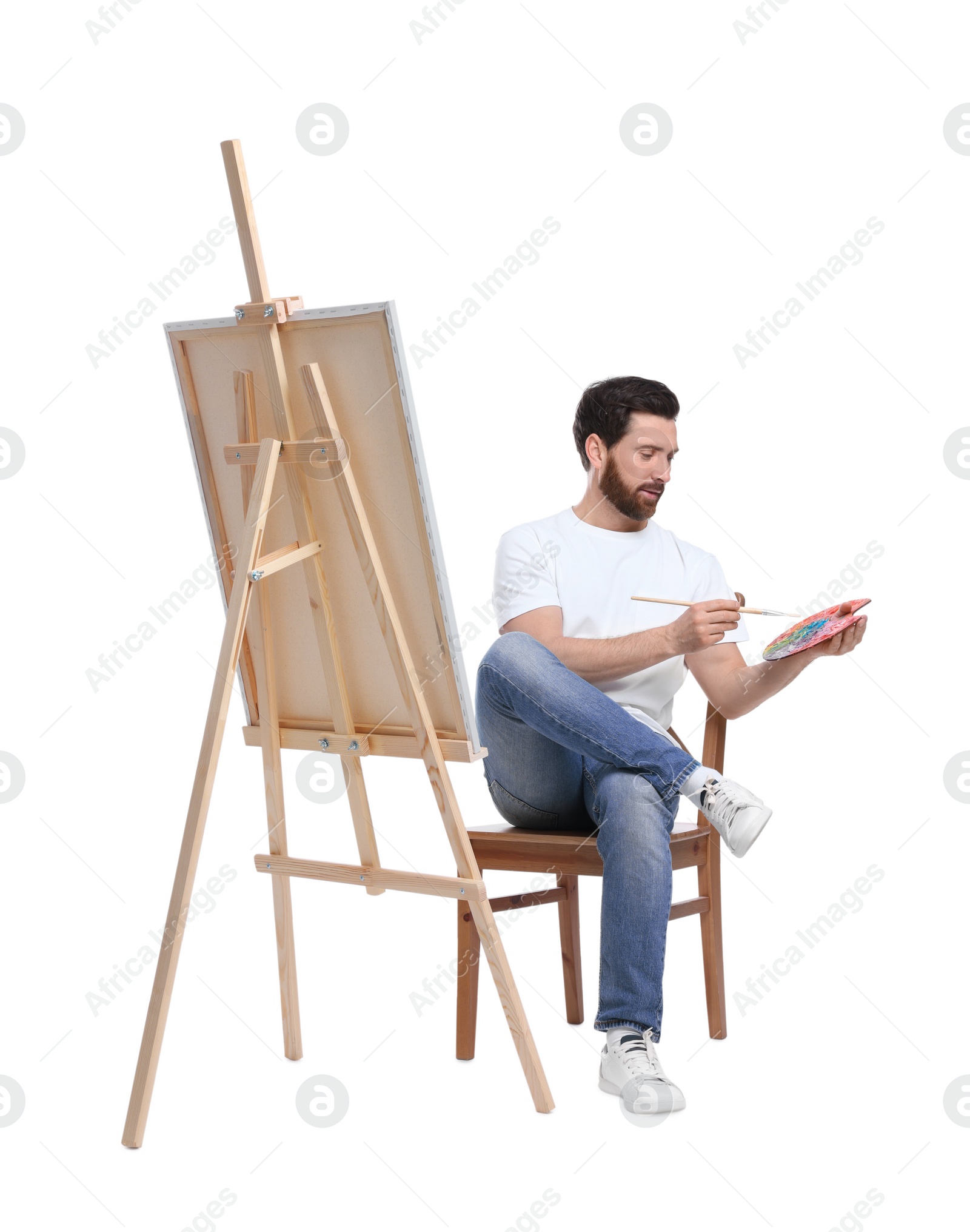 Photo of Man with brush painting against white background. Using easel to hold canvas