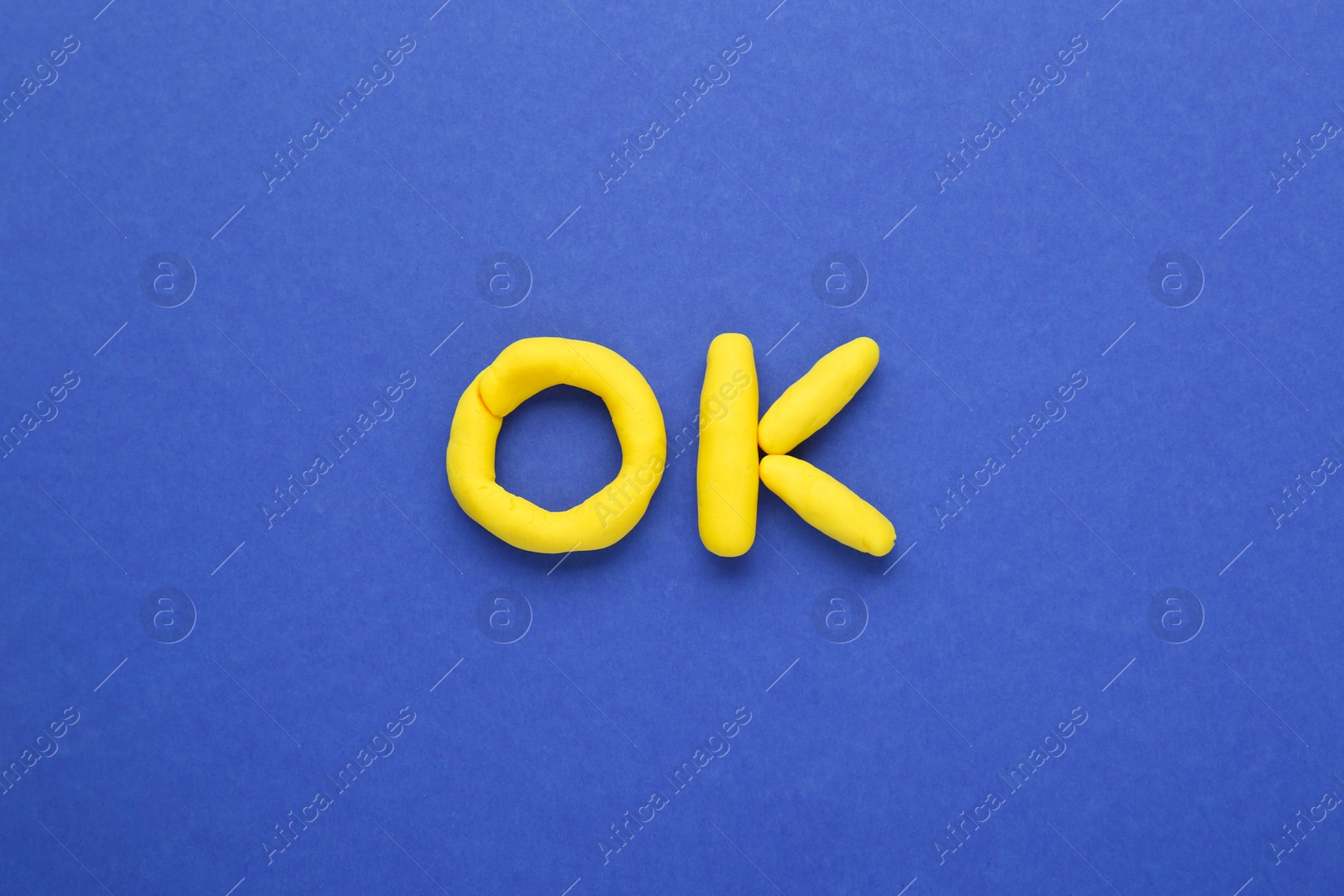 Photo of Word Ok made of yellow plasticine on blue background, top view