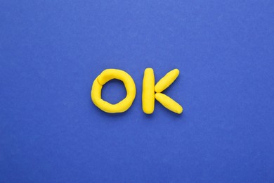 Photo of Word Ok made of yellow plasticine on blue background, top view
