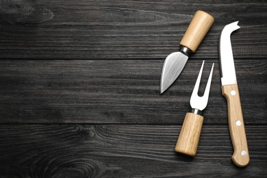 Cheese knives and fork on black wooden table, flat lay. Space for text