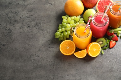 Photo of Different juices in mason jars and fresh fruits on gray table. Space for text