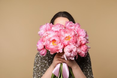 Photo of Young woman covering her face with bouquet of peonies on light brown background
