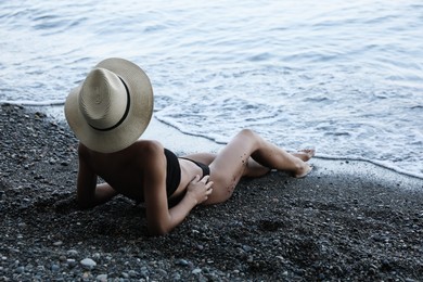 Young woman in stylish bikini and straw hat lying on seashore