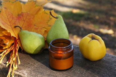Photo of Burning candle, tasty fruits and beautiful dry leaves on wooden surface outdoors. Autumn atmosphere