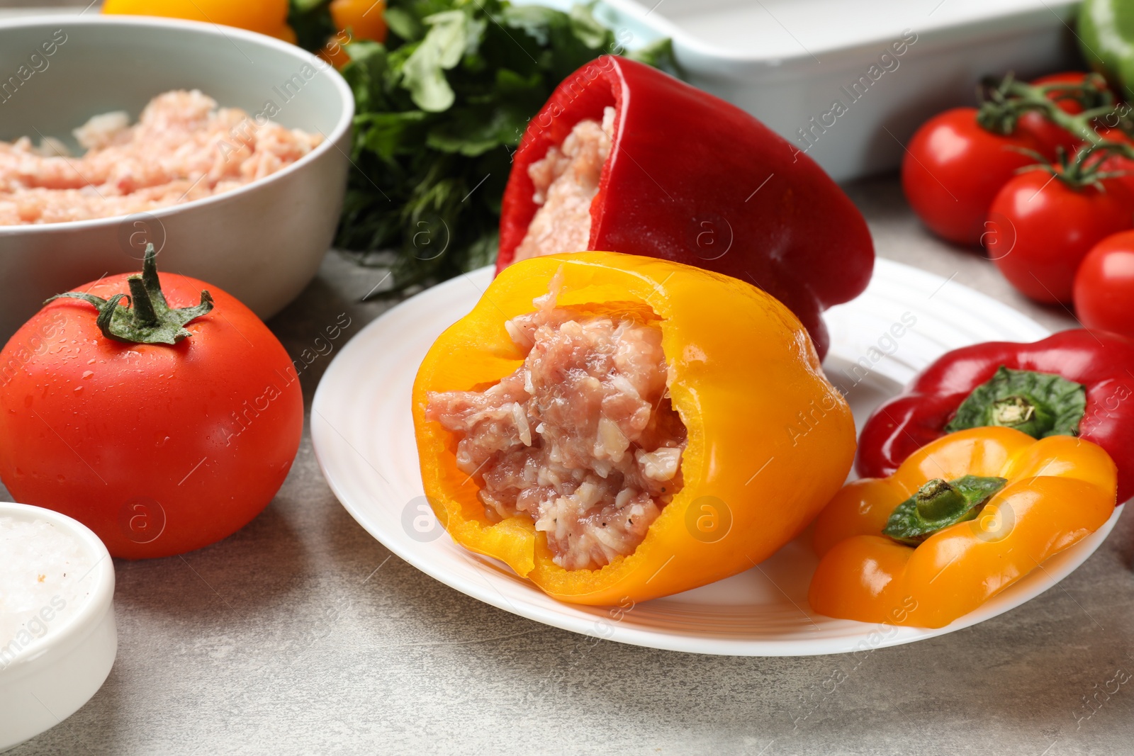 Photo of Raw stuffed peppers, ground meat and ingredients on grey table, closeup