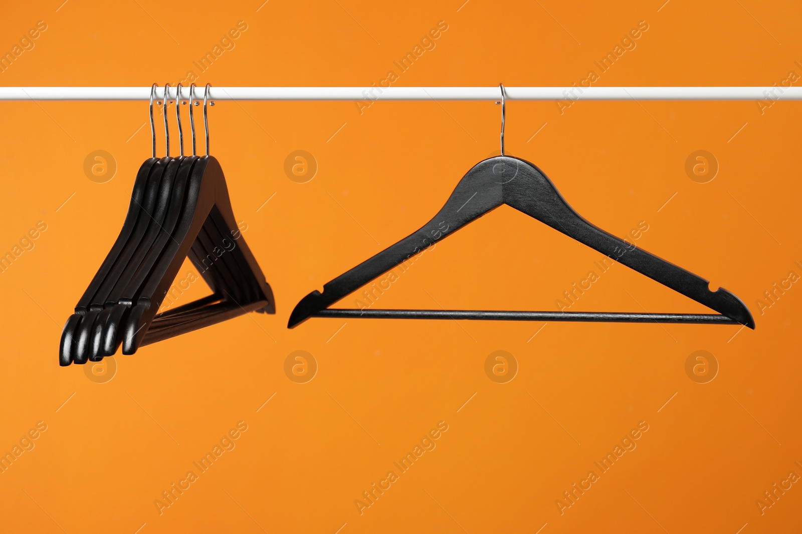 Photo of Black clothes hangers on rack against orange background