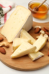 Photo of Tasty Camembert cheese with honey and nuts on white table