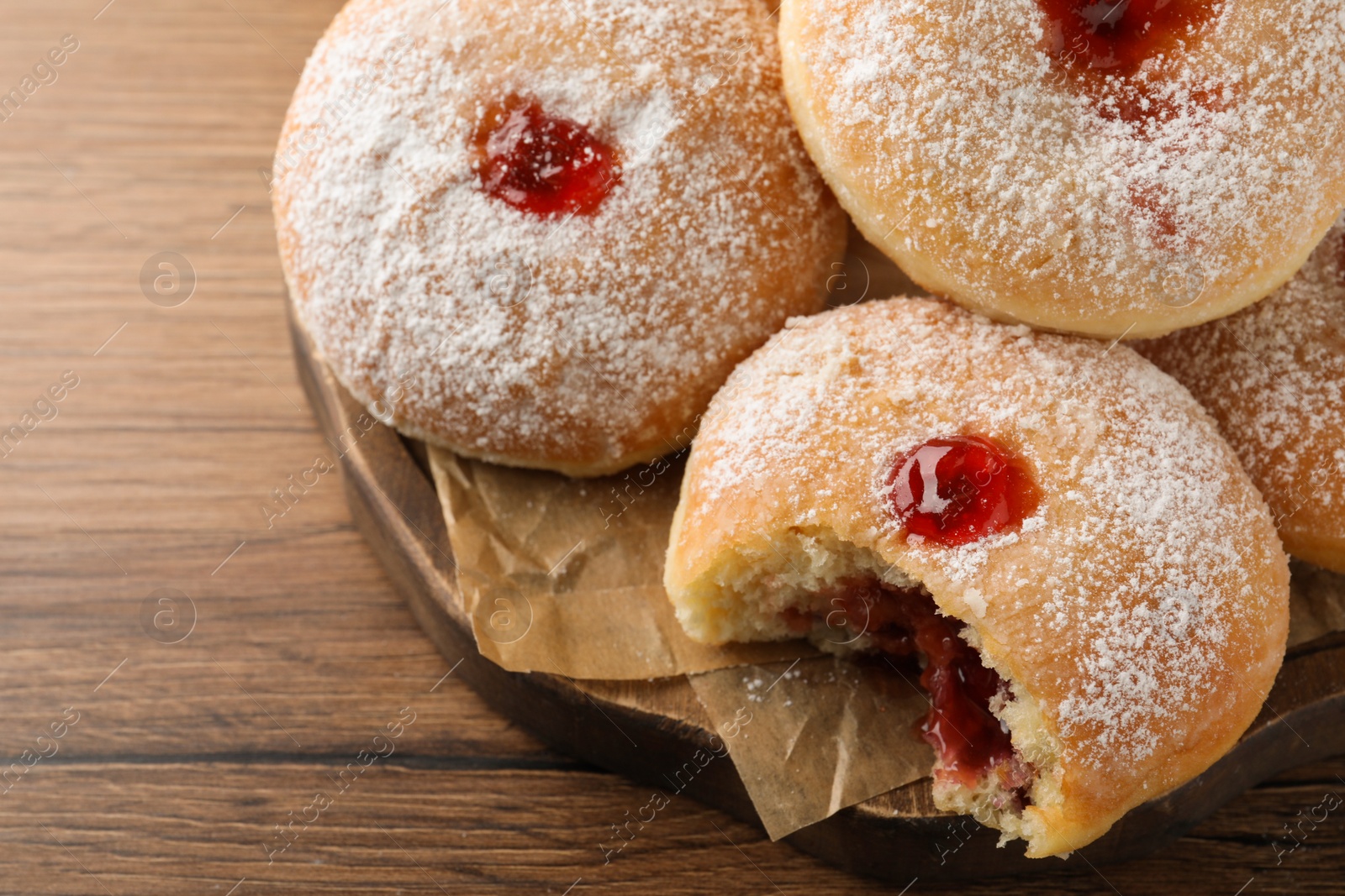 Photo of Delicious donuts with jelly and powdered sugar on wooden table, closeup