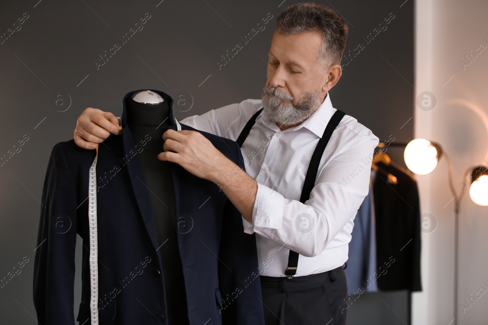 Photo of Mature tailor taking measurements of jacket on mannequin in atelier