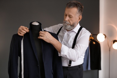 Mature tailor taking measurements of jacket on mannequin in atelier