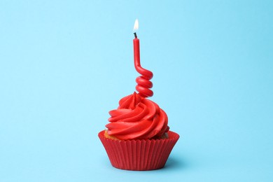 Delicious birthday cupcake with red cream and burning candle on light blue background