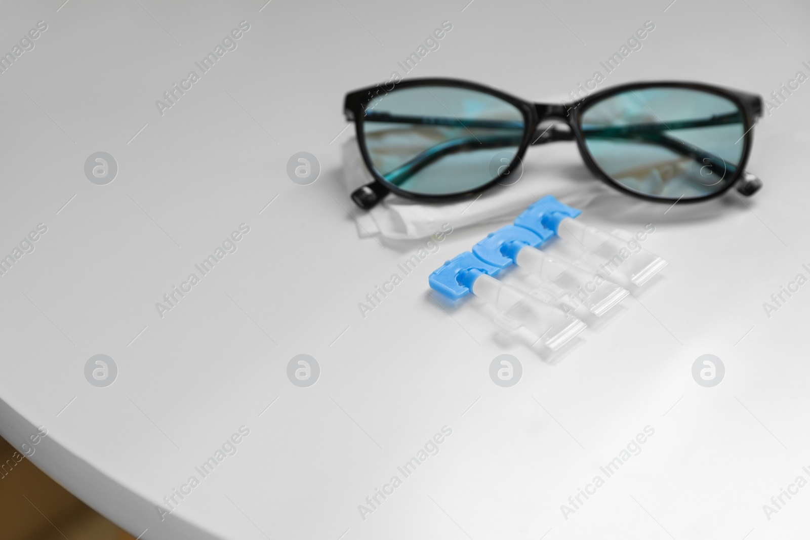 Photo of Single dose eye drops, glasses and fabric on white table, space for text