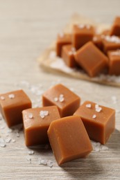 Tasty caramel candies and sea salt on light wooden table, closeup