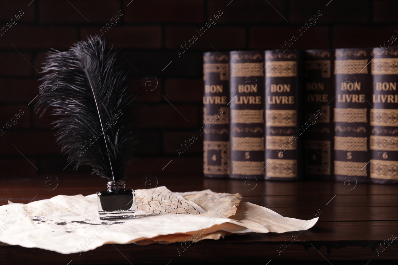 Photo of Inkwell with feather and vintage parchments near books on wooden table against black background