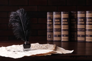 Inkwell with feather and vintage parchments near books on wooden table against black background