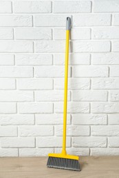 Plastic broom near white brick wall indoors