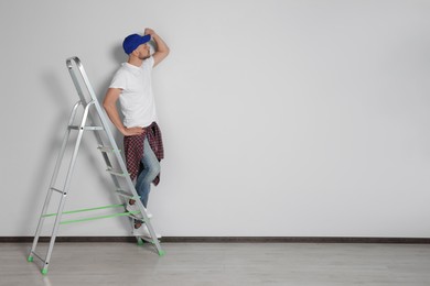 Photo of Handsome man on ladder near white wall indoors, space for text