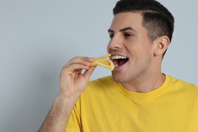 Man eating French fries on grey background, space for text