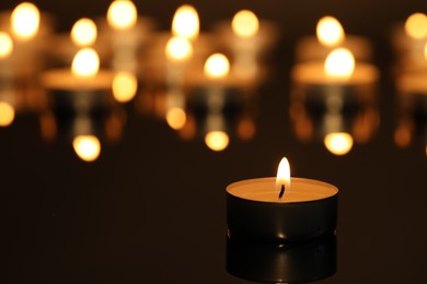 Photo of Burning candle on surface in darkness, closeup. Space for text