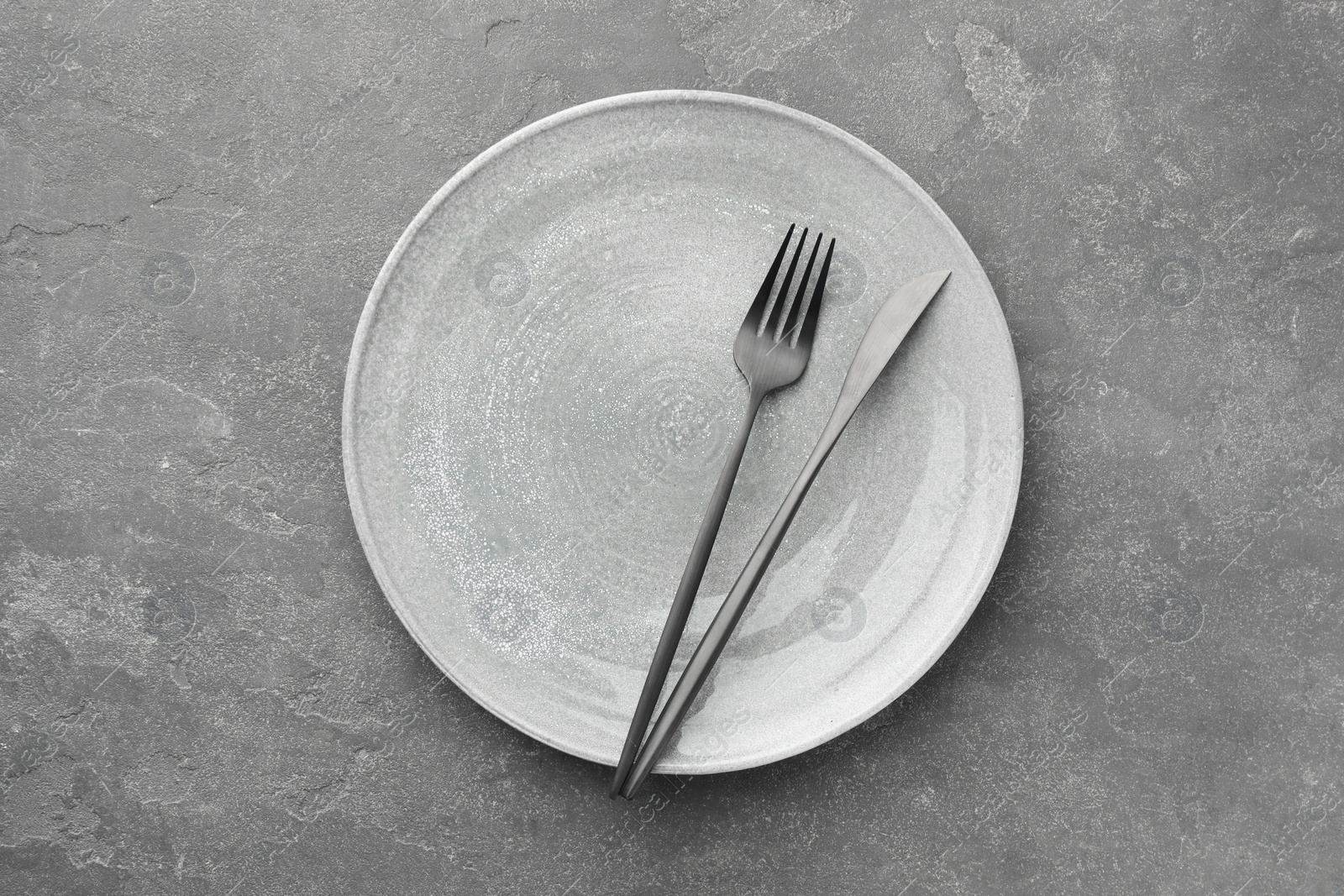 Photo of Clean plate, fork and knife on grey textured table, top view