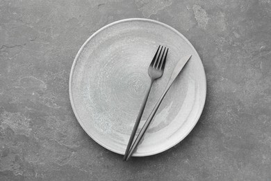 Clean plate, fork and knife on grey textured table, top view