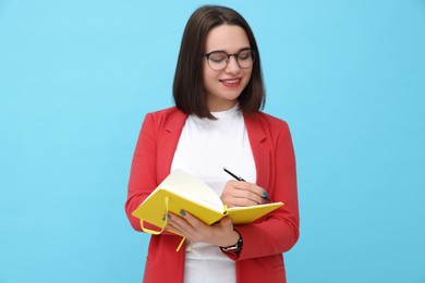 Photo of Happy young intern with notebooks and pen on light blue background