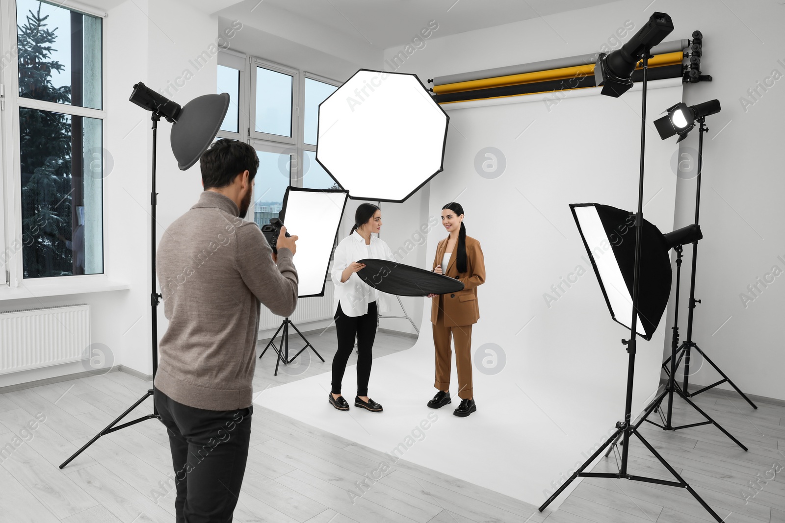 Photo of Professional photographer and assistant working with beautiful model in modern photo studio