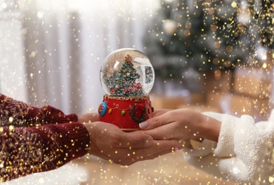 Image of Couple holding snow globe with Christmas tree at home, closeup