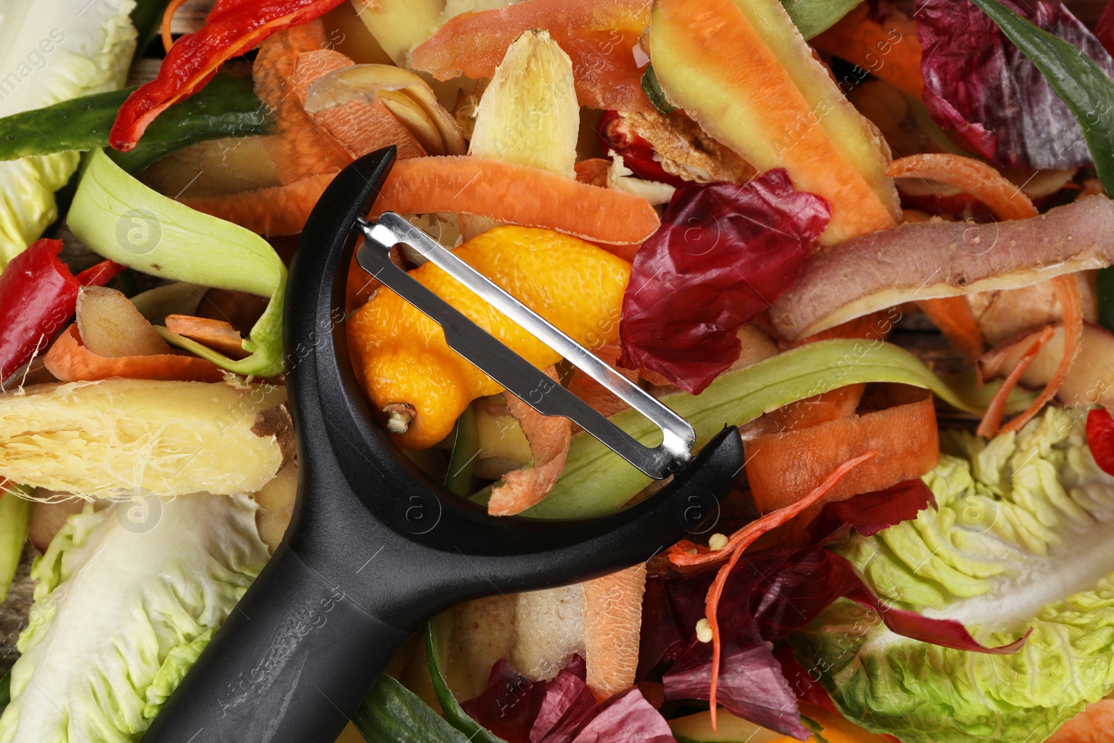 Photo of Peels of fresh vegetables and peeler on table, top view