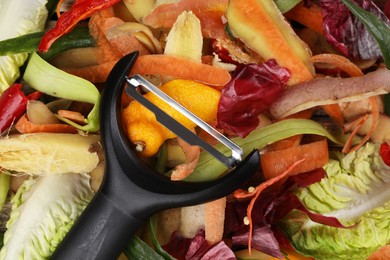 Peels of fresh vegetables and peeler on table, top view