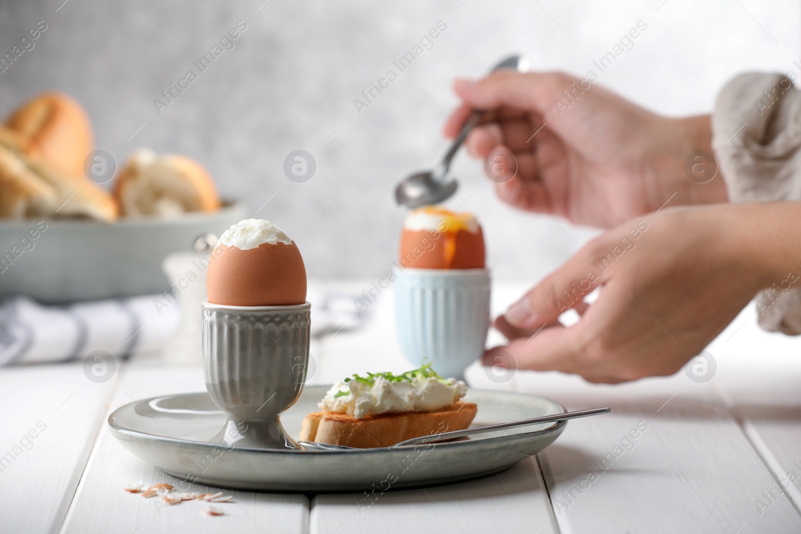Photo of Woman eating breakfast with fresh soft boiled egg at white wooden table, focus on plate