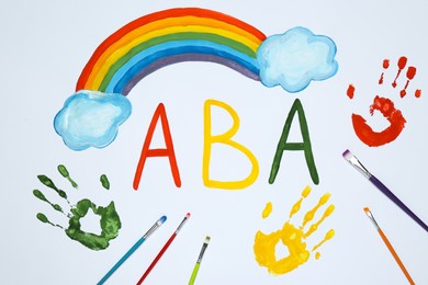 Photo of Drawn abbreviation ABA (Applied behavior analysis), rainbow, palm prints and paintbrushes on white paper, flat lay